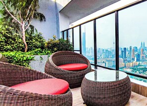 A balcony with wicker furniture and a glass table, overlooking a cityscape. - Luxury Balcony at Trion 1 KL by HCK (Kuala Lumpur)