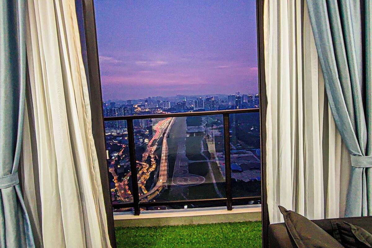 Blick aus einem Fenster mit Vorhängen auf eine Stadtlandschaft mit Gebäuden und einer Straße.