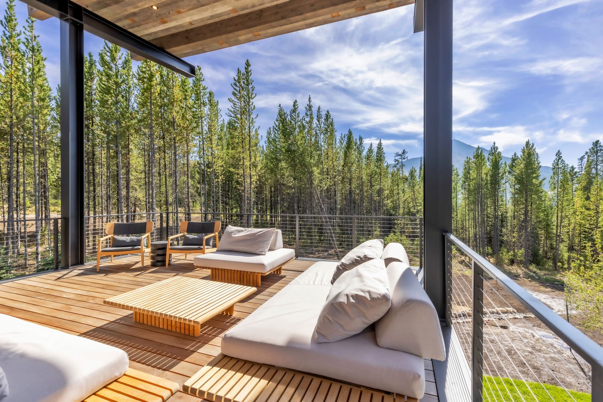A wooden deck with outdoor seating, including sofas and chairs, overlooking a forested area.