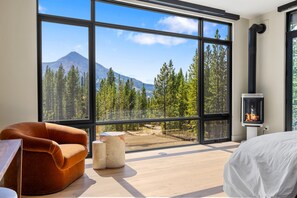 A bedroom with a large window, a fireplace, and a view of a forest and mountain.