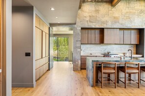 A modern kitchen with a stone accent wall, wooden cabinets, and a large island with bar stools. - Ski-In/Ski-Out | In-Ground Hot Tub (Big Sky)