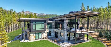 Una casa moderna de dos pisos con fachada de piedra, amplios ventanales y un amplio patio exterior.