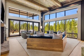 A spacious living area with a large sofa, multiple seating options, and a view of a forest through large windows.