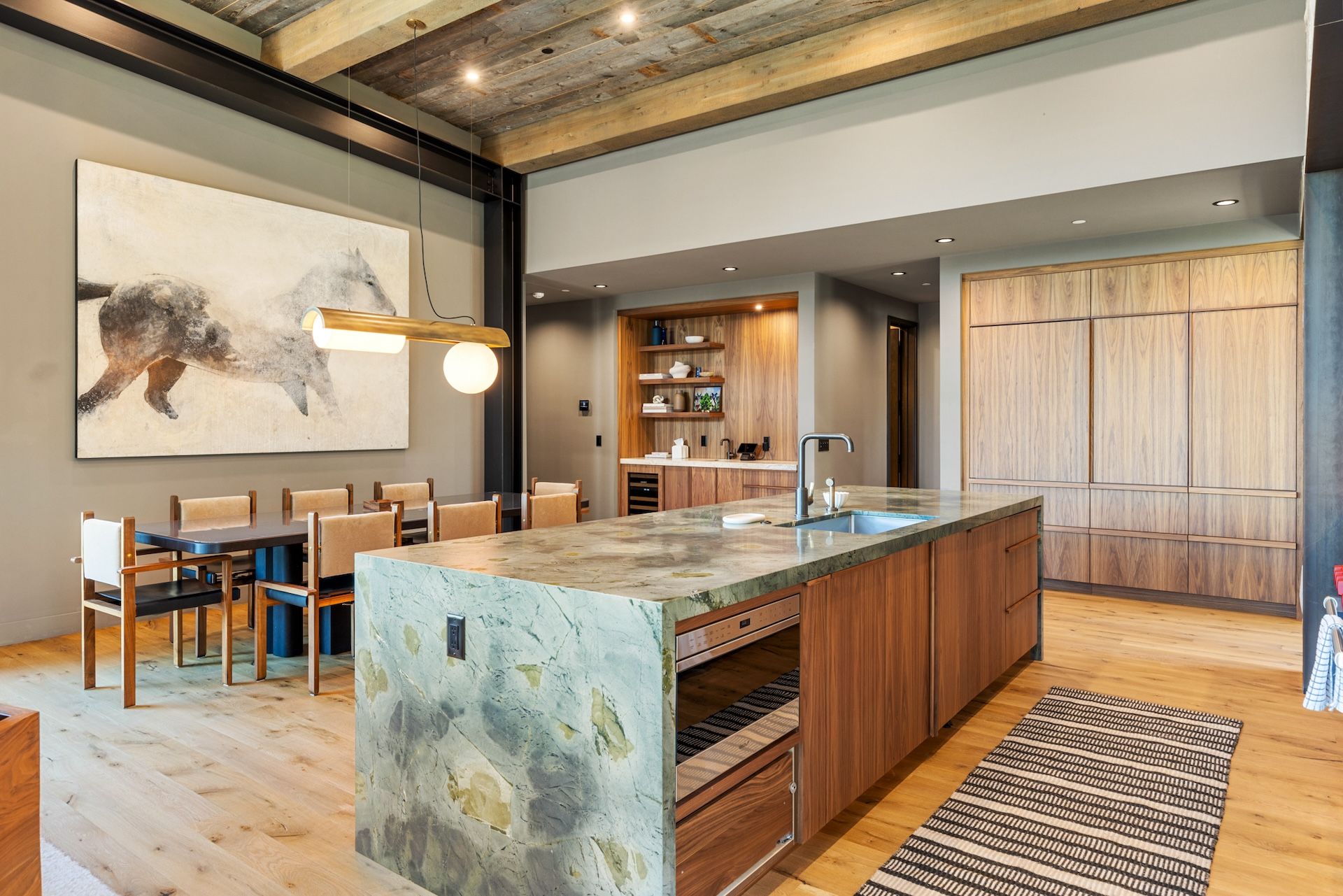 A modern kitchen with a marble island, wooden cabinetry, and a dining area with chairs.