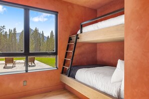 A bunk bed room with a view of a forest and a picnic table outside.