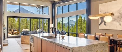 Una cocina moderna con una isla grande, armarios de madera y ventanas amplias con vistas a la montaña.