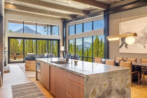 A modern kitchen with a large island, wooden cabinets, and large windows offering mountain views.