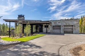 A modern two-story house with a stone facade, a covered patio, and a driveway leading to a garage. - Ski-In/Ski-Out | In-Ground Hot Tub (Big Sky)