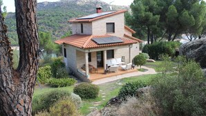 A two-story house with a tiled roof, a patio with outdoor furniture, and a garden with various plants and trees.