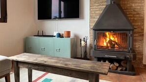 A living room with a television mounted on the wall, a stone fireplace, a teal cabinet, and a wooden bench.