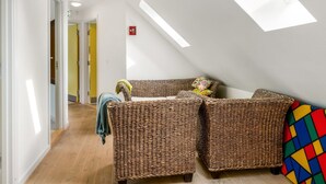 Une pièce avec un plafond en pente, un ensemble de meubles de salon en osier et un plaid aux couleurs vives.