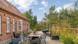 Une terrasse avec un bâtiment en briques, du mobilier d’extérieur et un espace barbecue.