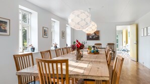 Un vaste espace dédié à la salle à manger, avec une longue table en bois, de nombreuses chaises et un luminaire au plafond au design original.