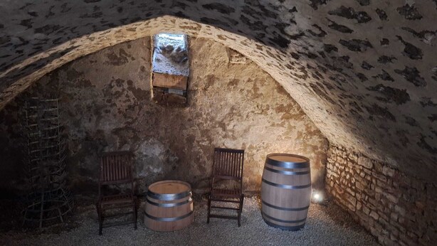 Una bodega rústica con paredes de piedra, barriles de madera y un pequeño estante de madera.