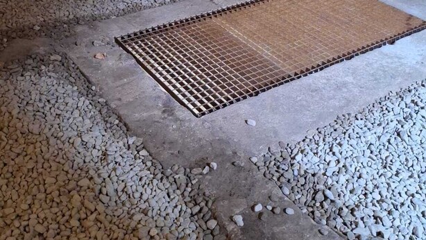Una bodega rústica con barriles de madera, paredes de piedra y un piso de concreto con grava.