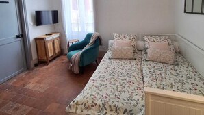 Un dormitorio con cama, televisión, ventana con cortinas, silla y armario.