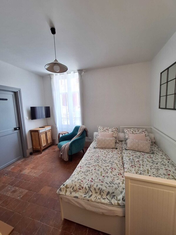 A bedroom with a bed, a TV, a window with curtains, a chair, and a cabinet.