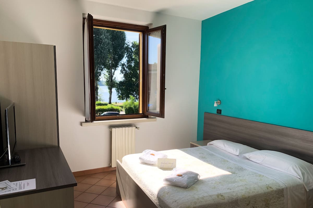 A bedroom with a bed, a desk, a window with a view of trees and a car, and a teal accent wall.