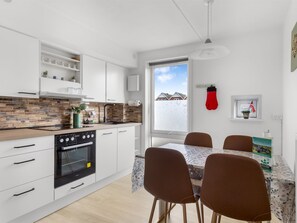 A modern kitchen with white cabinets, a black stove, and a dining area with a table and chairs.