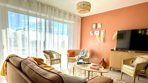 A living room with a brown sofa, wicker chairs, a coffee table, and a TV. - Villa l'Escale with large garden (Daubeuf-Serville)