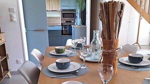 A dining area with a wooden table set for four, including plates, bowls, glasses, and cutlery. A vase with branches is on the table, and a staircase is visible in the background. - Villa l'Escale with large garden (Daubeuf-Serville)