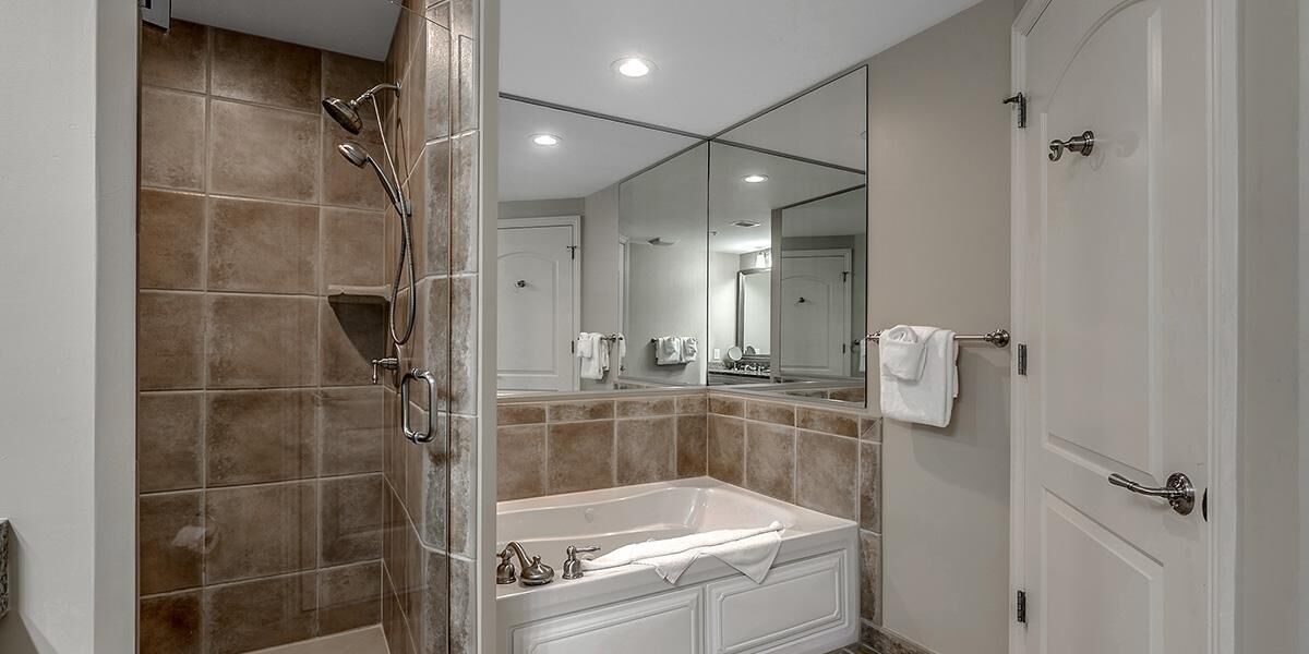 A bathroom with a bathtub, a shower, a large mirror, and a door.