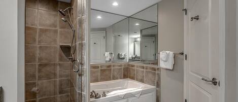 A bathroom with a bathtub, a shower, a large mirror, and a door.