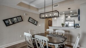 Un comedor con una mesa redonda y sillas blancas, una cocina con electrodomésticos de acero inoxidable e iluminación colgante.