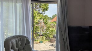 A room with a leather armchair, a flat-screen TV, and a sliding glass door leading to a patio with a garden view.