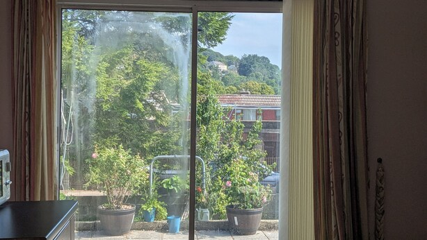 A room with a sliding glass door leading to a balcony with potted plants and a view of a residential area.