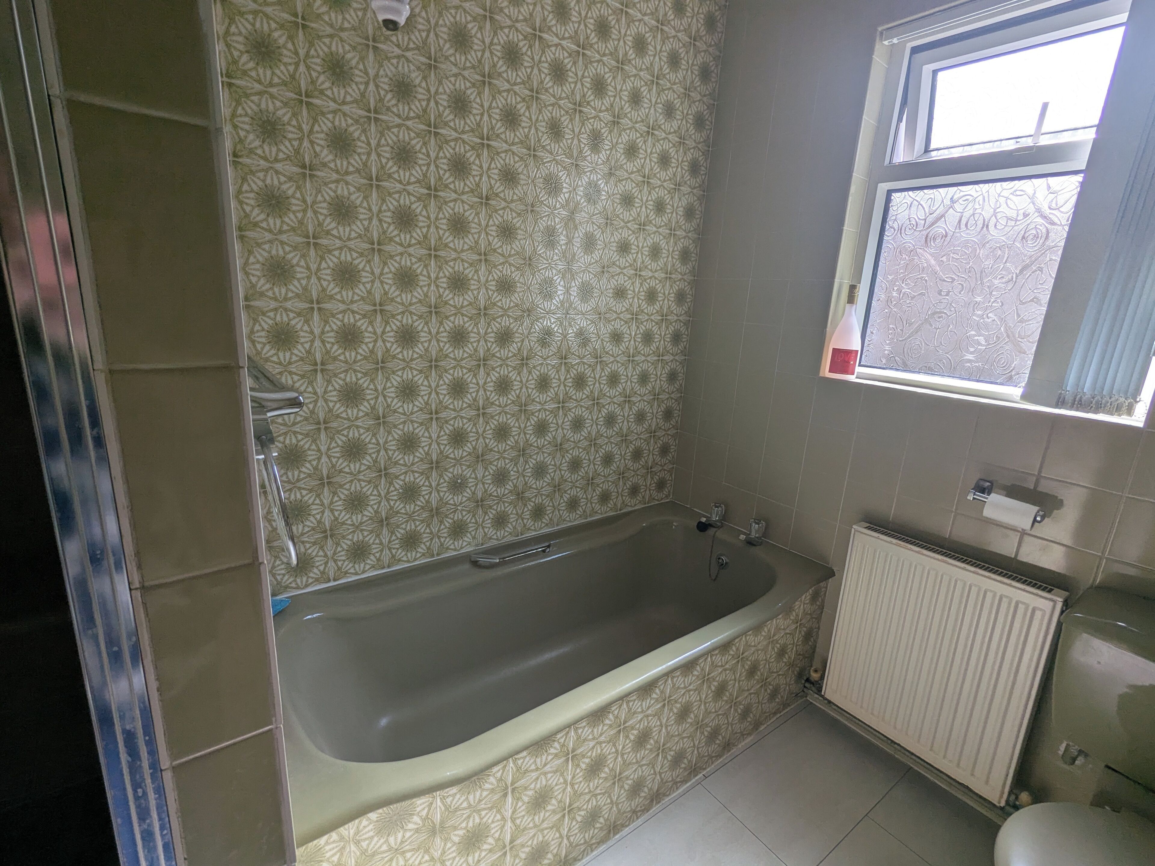 A bathroom with a freestanding bathtub, patterned tiles, a window, and a radiator.
