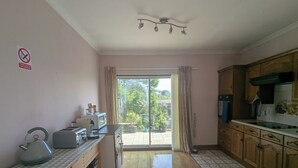 A kitchen with wooden cabinets, a microwave, and a kettle on the counter. There is a sliding glass door leading to a balcony with potted plants.
