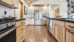 A modern kitchen with wooden cabinets, stainless steel appliances, and a stone accent wall. - Lunar Lodge on Windfall Lake (Exeland)