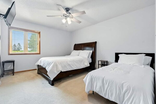 A bedroom with two single beds, a ceiling fan, a TV, and a window with blinds.