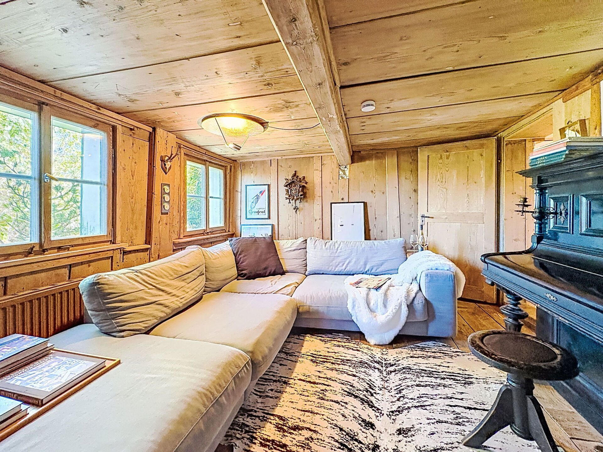 A cozy cabin interior with a wooden ceiling, a sofa, a table, and a fireplace.
