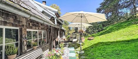 A rustic outdoor seating area with a table set for dining, a large umbrella, and a view of a traditional building.