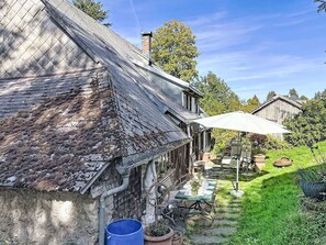 A rustic house with a thatched roof, a wooden porch, and a garden with outdoor furniture.