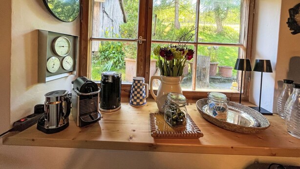 A kitchen counter with coffee makers, a clock, and a window with a view of the garden. - Beautiful private villa for 6 guests with terrace (Altglashütten)