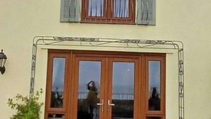 Una casa de dos pisos con techo oscuro, paredes de color claro y un balcón con barandilla de metal.