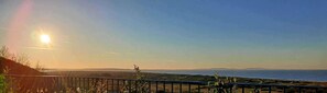 A coastal landscape with a clear sky and the sun low on the horizon, suggesting a sunrise or sunset. - Bayview Cottage Escape in Pendine (Carmarthen)