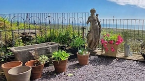 Una estatua en un balcón con vistas al mar, rodeada de macetas y una valla de metal.