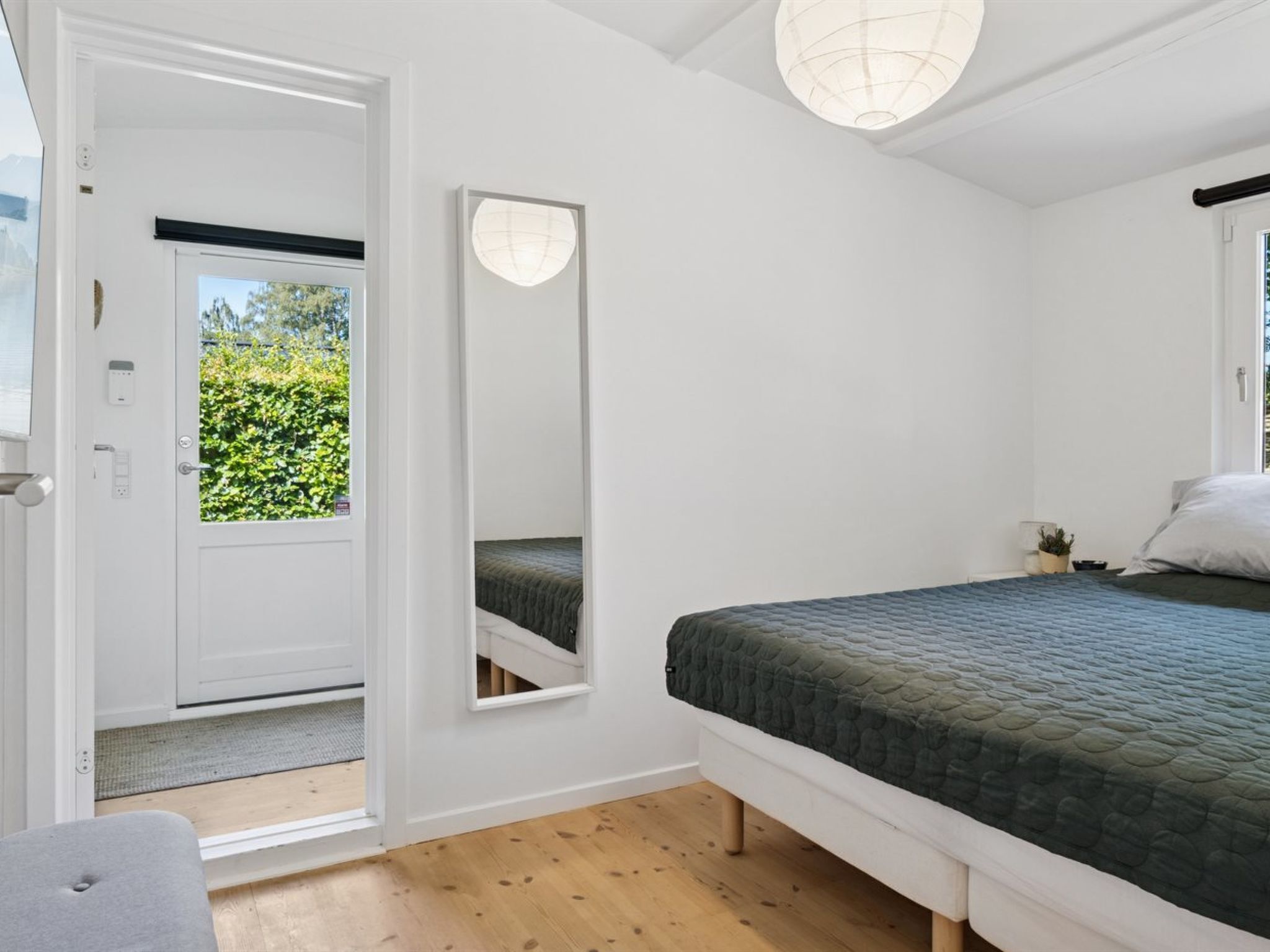 Een slaapkamer met een bed, een deur naar een balkon, een spiegel en een plafondlamp.