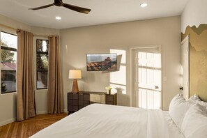A bedroom with a bed, a nightstand with a lamp, a wall-mounted TV, and a door.