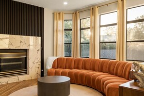 A living room with a curved sofa, a fireplace, and large windows with curtains.