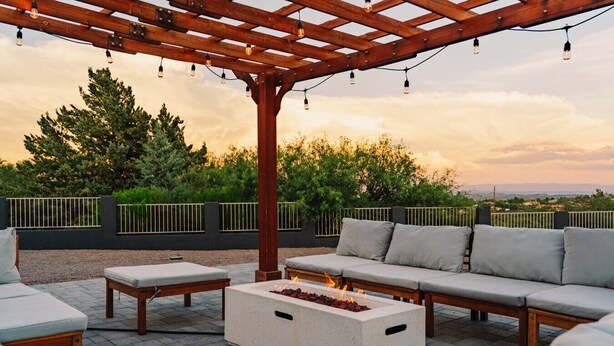 Ein Außenbereich mit Sitzgelegenheit, einer Pergola, einem Feuerbereich und Blick auf die Landschaft.