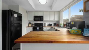 A modern kitchen with white cabinets, a black refrigerator, a microwave, and a wooden countertop.