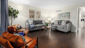 A modern living room with two grey sofas, a brown leather armchair, a small round coffee table, and a large potted plant.
