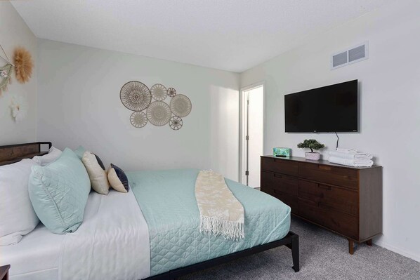 A bedroom with a bed, a dresser, a flat-screen TV, and wall decor.