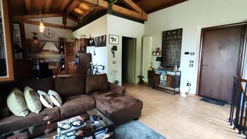 A cozy living room with a brown sectional sofa, a glass coffee table, and a kitchen area with wooden cabinets and a refrigerator.