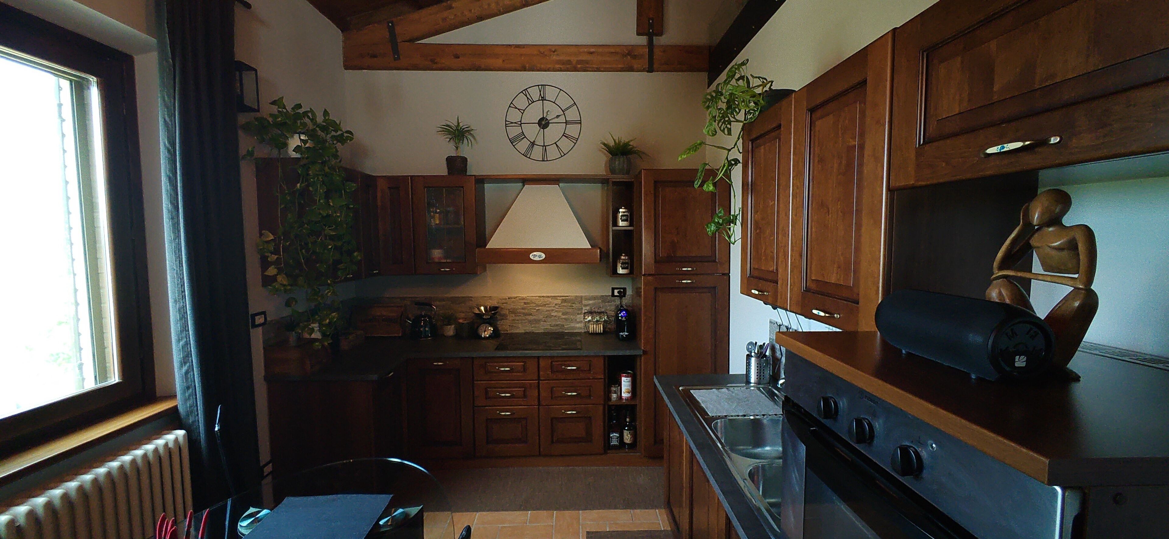 Een keuken met houten kastjes, een klok en verschillende planten.